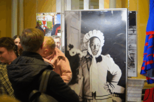 widzowie wernisażu oglądają wystawę, w tle wisząca fotografia