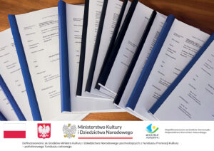 Stos dokumentacji projektowej w białych i niebieskich oprawach leżący na drewnianym blacie. Na pierwszej stronie widoczny tytuł Projekt Techniczny dotyczący przebudowy lokalu Wojewódzkiej Biblioteki Publicznej w Olsztynie. Poniżej belka informacyjna.